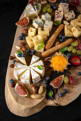 Wooden board with different types of cheese, nuts, berries and fruits.