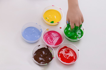 Bottles with colorful finger paint in a white background and a kid hand getting paint in his fingers. Little Artist