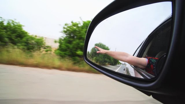 Mirror reflection of male hand holding out of moving car from the window. Enjoying high speed movement. Traveling, comfortable lifestyle concept.
