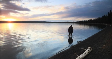 Yellowstone sunset woman wade in forest lake. Beautiful sunset over high Rocky Mountain lake. Nature, serenity and peace landscape environment. Geography, geology, natural beauty.