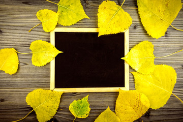 Colorful yellow autumn leaves on wooden table and blackboard