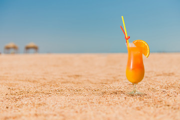 cocktail with orange juice on sandy beach line at seascape on horizon