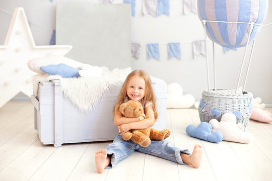 Smiling little blond girl hugs a teddy bear on the background of a decorative balloon. The child plays in the children's room with toys. The concept of childhood, travel. birthday, holiday decorations