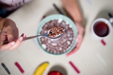 spoon of chocolate cereal with milk over the table. Table with a plate and a mug in defocus, top view