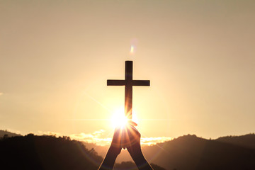 human hands praying to the GOD while holding a crucifix symbol with bright sunbeam on the sky
