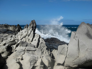 Waves crashing with spray against lava flow formation known as dragon's teeth on Maui Hawaii with blue sky background 