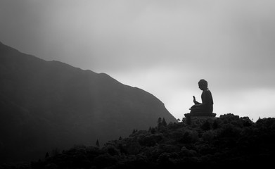 Silhouette of buddha statue along ridgeline above trees against cloudy sky backdrop in Hong Kong 