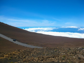 vehicle driving up a road at high altitude above the clouds on a road surrounded by volcanic ash and debris with blue sky background 