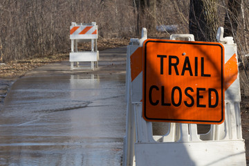Trail closed signs posted near flooded paved hiking trail