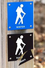 Hiking trail markers for winter and summer access with the summer sign cracked through the word summer
