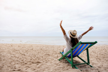 A female traveler with hat opening arms while sitting on the beach chair by the sea