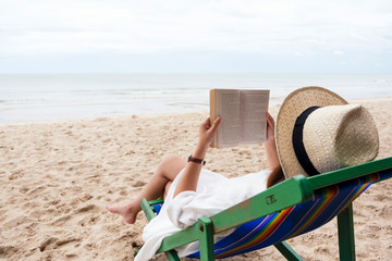 A beautiful woman lying down and reading book on the beach chair with feeling relaxed