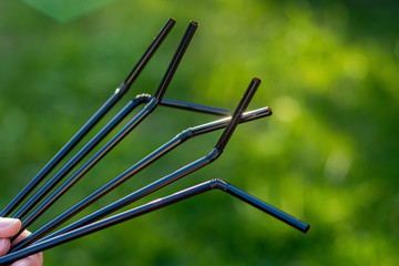 Hand holding black plastic straws on green grass background. Plastic pollution, environmental waste. Say no to plastic straw. Save our planet