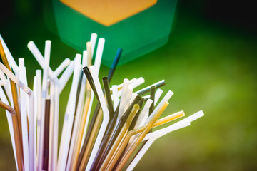 White, black and gold plastic straws on green grass background. Plastic pollution, environmental waste. Say no to plastic straw