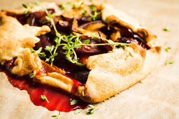Freshly baked tart with plums and thyme on the rustic background. Selective focus. Shallow depth of field.