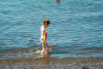 Little girl in a swimsuit bathing in the sea in summer, making a splash and running in water