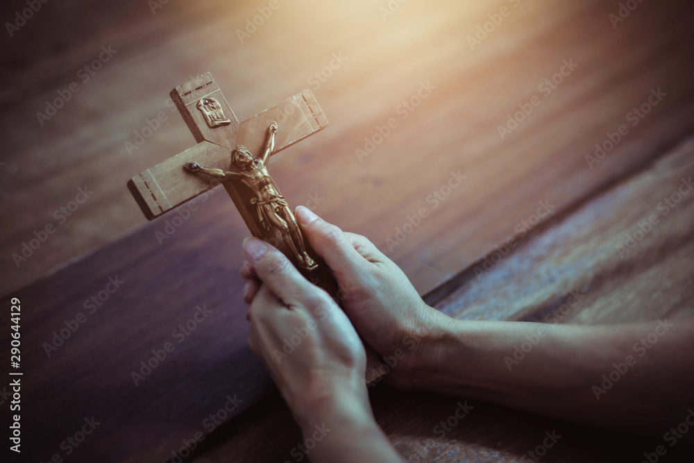 Wall mural close up of woman hands holding crucifix of jesus christ while praying to god on wooden table backgr