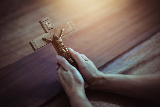 Close up of woman hands holding crucifix of Jesus Christ while praying to God on wooden table background, Christian trust and faith concept with copy space.