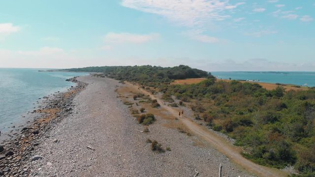 A couple jogging together in beautiful landscape alongside a stone beach by the ocean in the summer - Aerial 4K