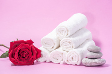 Obraz na płótnie Canvas White soft towels, red rose and stones for skin care and spa on a pink background