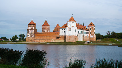 Fototapeta na wymiar Panorama of the castle in the city of Mir in Belarus. Castle against a cloudy sky with a bridge over a water channel.