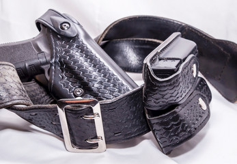 A worn police duty belt with a black pistol and two pistol magazine case wrapped up on a white background