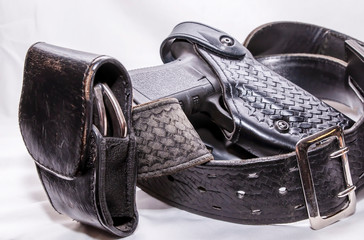 A worn police duty belt with a black pistol and handcuff case wrapped up on a white background