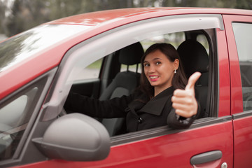 Fototapeta na wymiar Happy woman inside a car driving in the street and gesturing thumb up
