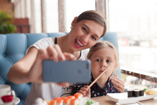 Mom and daughter are eating sushi and taking a selfie with her smart phone