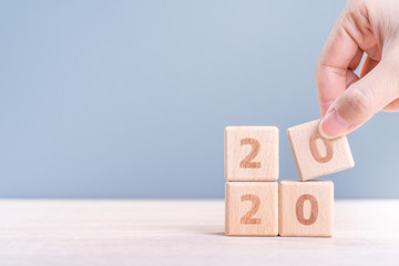 Abstract 2020 & 2019 New year countdown design concept - woman holding wood blocks cubes on wooden table and blue background, close up, copy space.