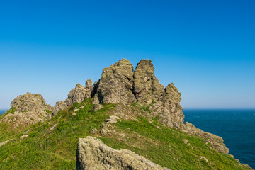 Rock formations protruding out of a green and grass hillside that overlooks the sea near Start Point Lighthouse on a clear day in England, UK.