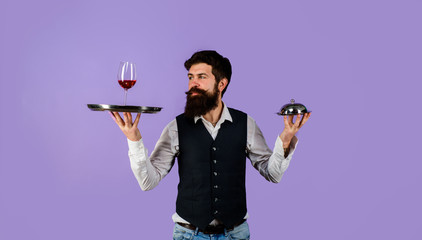 Handsome man waiter in uniform at restaurant. Waiter holds tray with wine and metal cloche lid cover. First class service concept. Best service. Professional catering service. Butler concept. Waiter.