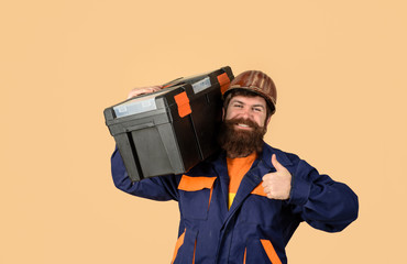 Builder man carrying tool box giving thumbs up. Repairman in overall hold toolbox. Man with tool box. Builder in protective helmet with toolbox. Tools for repair. Repair. Handyman concept. Repair kit.