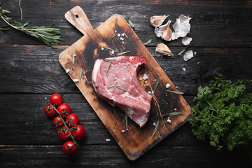 a raw piece of meat lies on the table, fragrant spices, tomatoes and herbs.