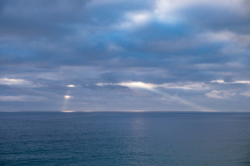 Naklejka na ściany i meble Sun rays shinning through the clouds above the horizon of the sea on a cloudy day in England, UK.
