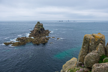 Rock formations in the sea and a lighthouse in the distance on this cloudy day in England, UK.
