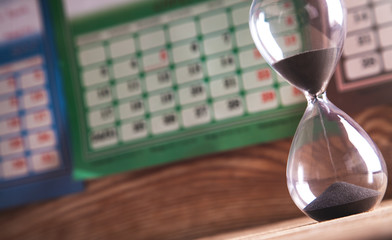 Hourglass on the wooden table in calendar background. Deadline concept