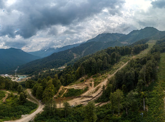 Fototapeta na wymiar construction of a ski slope on a mountainside covered with forest. Cloudy summer day, aerial view