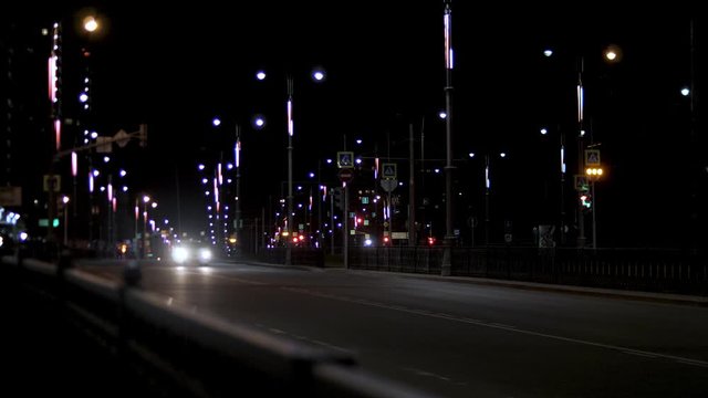 Night traffic on the road, lonely car driving along the street lamps. Stock footage. Night city road with street lights and moving car on dark sky background.