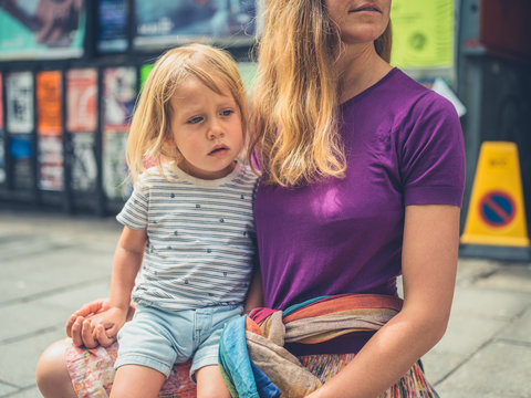 Millenial mother sitting on pavement with sad toddler