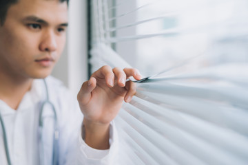 Shot of a young male doctor standing in doctor's room and looking through the window.
