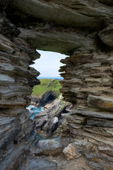 The a window from ruins of King Arthur’s Castle provides a view of the green and rocky cliffs that overlook the sea.