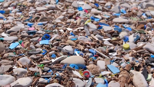 Plastic waste covers and garbage on pebble at seashore after storm, closeup view. Plastic litter garbage waste rubbish on ocean beach. Environmental pollution ecology disaster damage problem.