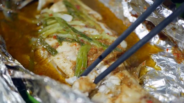 Tourists eat fish by chopsticks cooked in foil at Asian street food market. Closeup