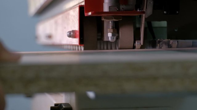 Machine for gluing edges on chipboard parts. Furniture manufacture. Shallow depth of field, selective focus. The mechanism of automatic movement of the rollers on the machine.