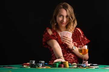 A girl in an evening red dress plays poker raising the stakes with chips. Gaming business in a casino or night club.