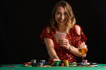 A girl in an evening red dress plays poker raising the stakes with chips. Gaming business in a casino or night club.