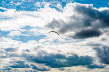 A paraglider with a yellow parachute can be seen flying through the air on partially cloudy day in England, UK.