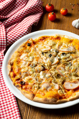 Fresh homemade pizza with ham, mushrooms and olive on a wooden background in composition with a red cloth and olive oil. Italian Cuisine. Selective focus on center of pizza