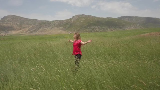 A young girl happily dancing in slow motion in the green field, touching the ears of wheat by hand